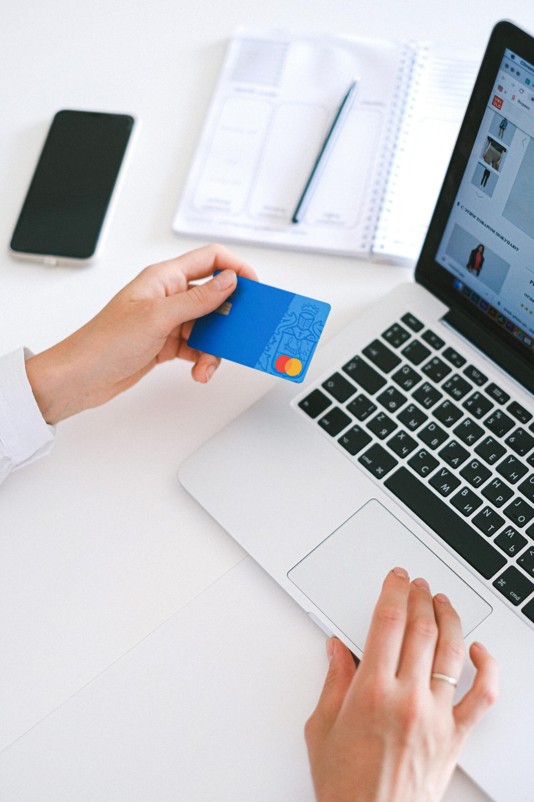 Two hands holding a credit card in front of a laptop screen to pay at an online shop